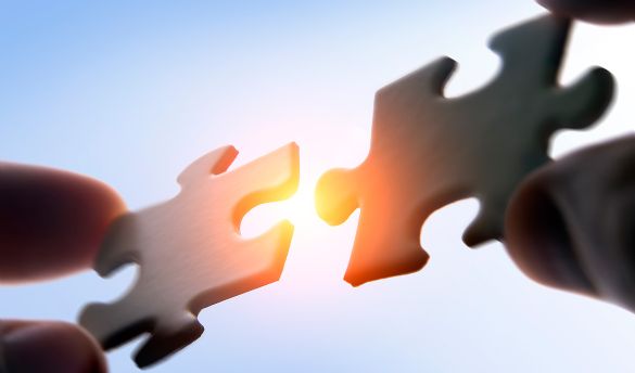 Zwei Hände halten zwei Puzzelteile in der Luft und versuchen diese zu verbinden