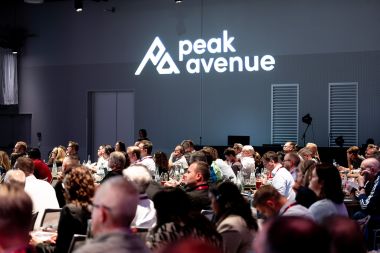 Gut gefüllter Plenarsaal mit Teilnehmenden der PeakAvenue Conference 2026 vor dem beleuchteten PeakAvenue Logo.