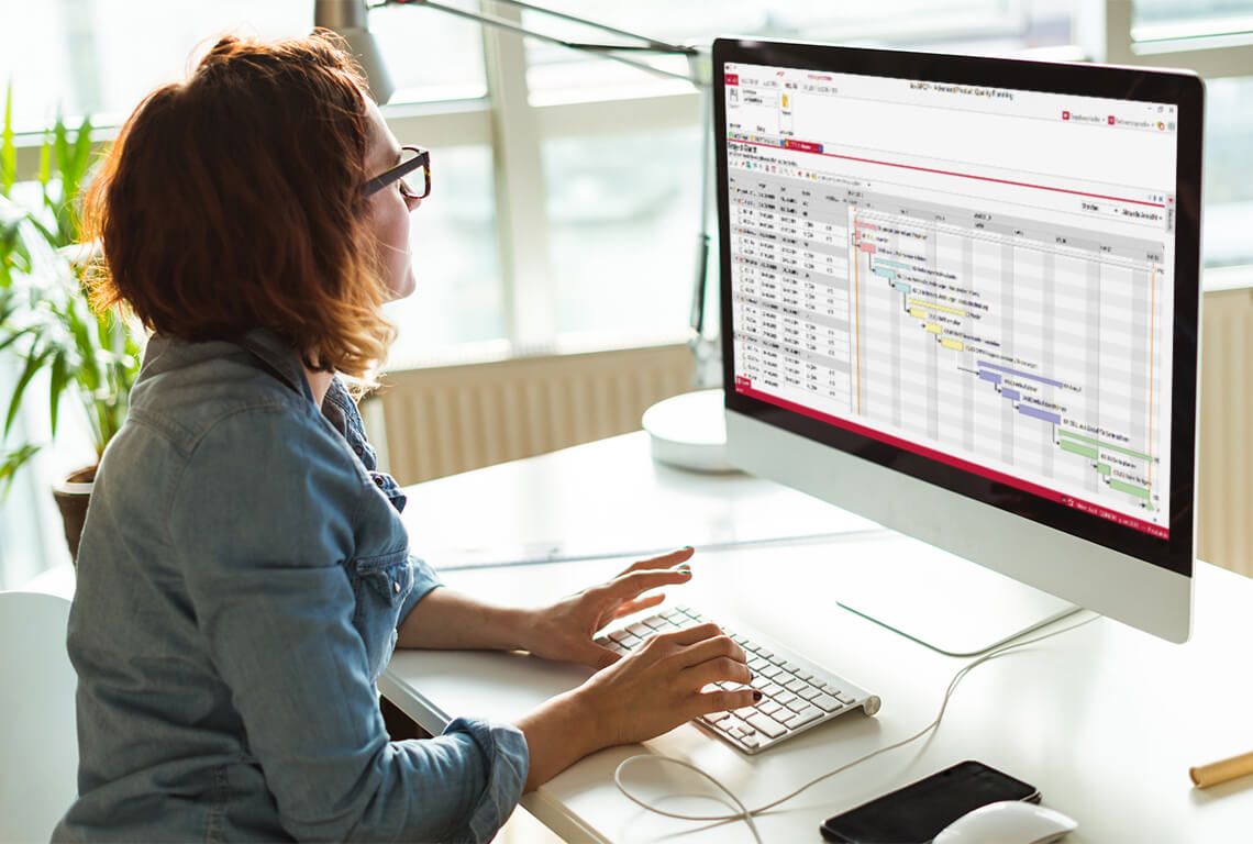 Frau sitzt vor einem Bildschirm und bearbeitet ein APQP Gantt-Diagramm