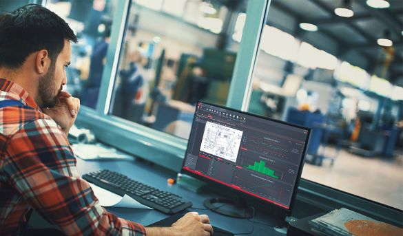 Qualitätsbeauftragter sitzt in Produktionshalle vor Laptop und bearbeitet Merkmalsliste
