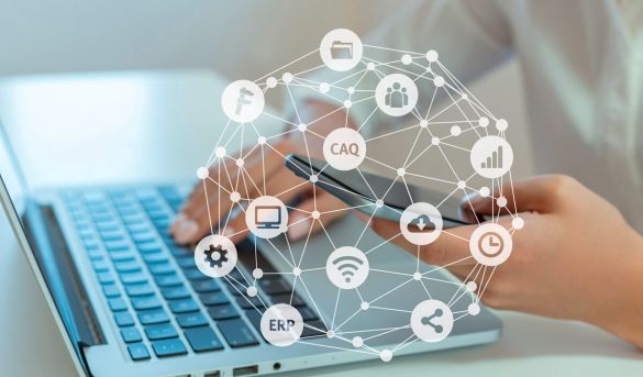 Netz mit verschieden Symbolen wie CAQ, ERP, Zahnrad, Cloud und im Hintergrund sitzt eine Frau mit Laptop und Handy in der Hand.